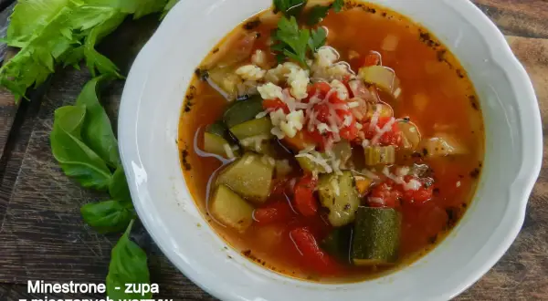 Miseczka zupy minestrone z warzywami i startym serem, obok łodygi selera i liście bazylii.