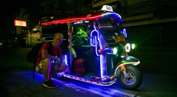 Uśmiechnięty turysta przy neonowym tuk tuk taxi w Tajlandii. Nocne światła tworzą magiczną atmosferę.