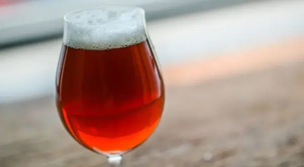 Un bicchiere di irish red ale con schiuma bianca, su un tavolo di legno.