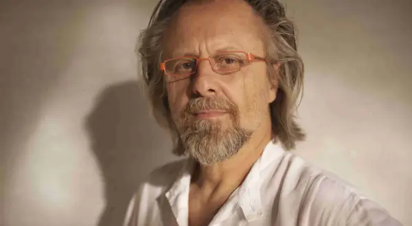Portret mężczyzny w okularach, jednego z polskich kompozytorów współczesnych, z siwiejącą brodą i włosami, w białej koszuli.