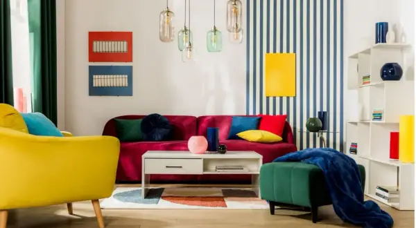 Salon w stylu memphis: żółty fotel, bordowa kanapa, kolorowe poduszki, geometryczny dywan i lampy.