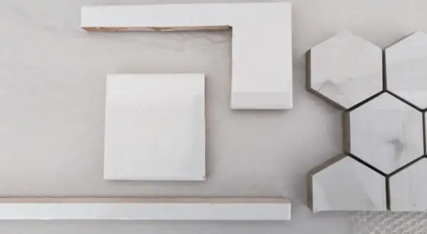 White wall tiles, including square, L-shaped, and hexagonal pieces, are laid out on a light surface, hinting at how to cut wall tile for a project.