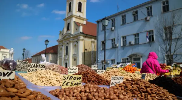 En marknad i Belgrad under en solig helg. Ett överflöd av nötter och torkad frukt säljs framför en kyrka och blå byggnad.