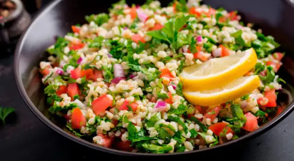 Delicioso tabule receta, una ensalada fresca de bulgur, tomate, perejil y cebolla morada, adornada con rodajas de limón.