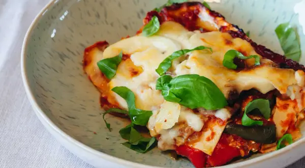 Ein Stück köstliche vegetarische Lasagne mit geschmolzenem Käse und frischem Basilikum in einer Schüssel.