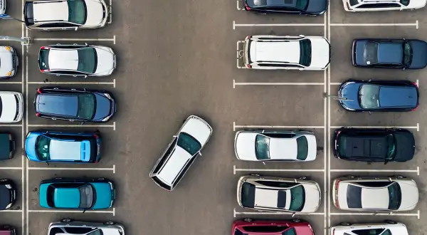 Widok z góry na parking, gdzie samochody zaparkowane są prostopadle. Widać różne kolory i modele aut.