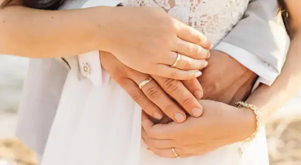 Manos entrelazadas con anillos de boda, mostrando dónde se pone el anillo de compromiso. Un detalle de amor eterno.