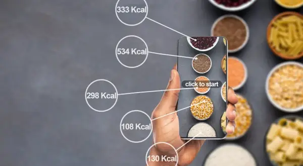 Dłoń trzyma smartfon z aplikacją do liczenia kalorii. Na ekranie widać różne produkty spożywcze i ich kaloryczność, pomocne przy diecie 1500 kcal.