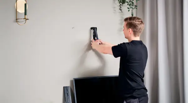 Uomo usa rivettatrice per rinforzare parete cartongesso, preparando il muro per un nuovo mobile.