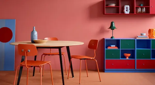 Ein Essbereich mit orangen Stühlen und einem Holztisch. Die Wand ist in einem warmen Rotton gestrichen. Ein rotes Wandregal und ein rotes Schubladenelement setzen Akzente.