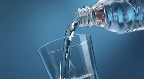 Un filet d'eau pure, riche en magnésium, se verse d'une bouteille dans un verre transparent sur fond bleu.