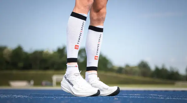 Manchons de compression mollet : pour une meilleure récupération et performance. Ces manchons blancs avec logo Compressport sont portés par un coureur.
