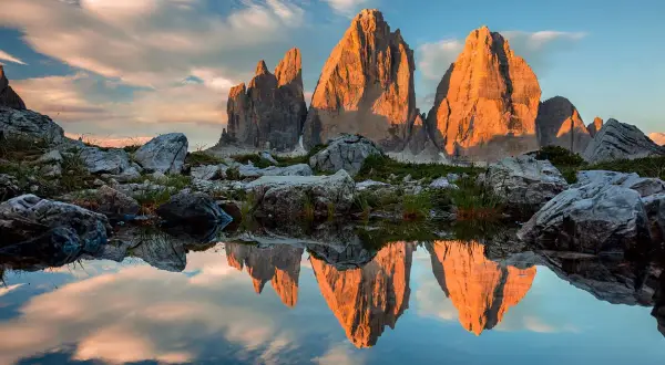 Le Tre Cime di Lavaredo illuminate dal tramonto, riflesse in uno specchio d'acqua. Le **dolomiti più belle** in uno scenario mozzafiato.