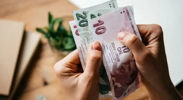 Ręce trzymają banknoty 10 i 20 lir tureckich. Planujesz podróż i zastanawiasz się, jaką walutę zabrać do Turcji? Lira turecka to odpowiedź!