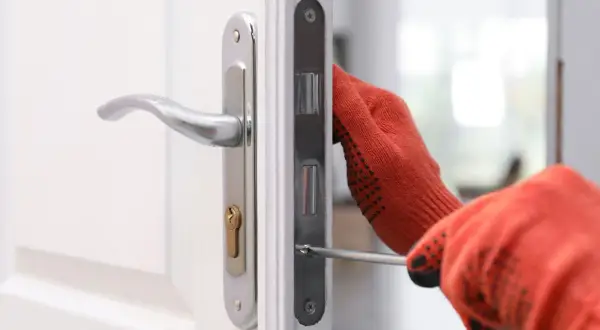 Main tenant utilise un tournevis pour changer la serrure d'une porte blanche.