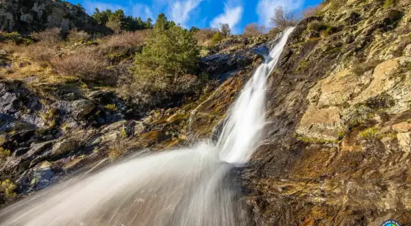 Cascada en un paisaje rocoso y seco, con vegetación escasa. El agua cae con fuerza, creando una estela blanca. Un rincón natural cerca de San Mamés, Madrid.
