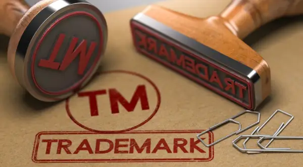 Dwa stemple z napisem "TRADEMARK" i symbolem "TM" na brązowym tle, obok spinaczy.