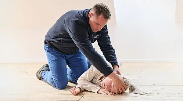 Mann übt die stabile Seitenlage an einer Person auf dem Holzboden.