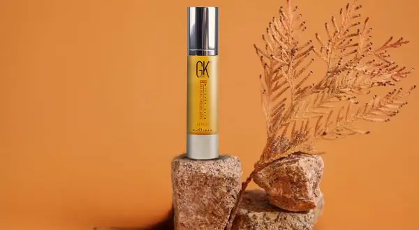 Sérum capilar GK Hair en envase dorado, con ramas secas y rocas. Descubre las maravillosas aceite de argan propiedades para tu cabello.