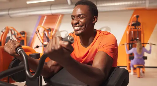 Un homme souriant s'entraîne pour muscler les bras sur une machine de musculation.