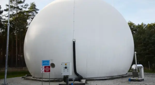 Ogromny, biały balon magazynujący biometan, otoczony drzewami. Obok znajduje się panel sterowania i rury.