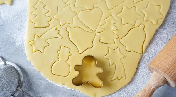 Ausgestochener Teig für Weihnachtsplätzchen mit Sternen, Herzen, Tannenbäumen und Schneemännern. Ein Ausstecher-Rezept für Spaß in der Küche.