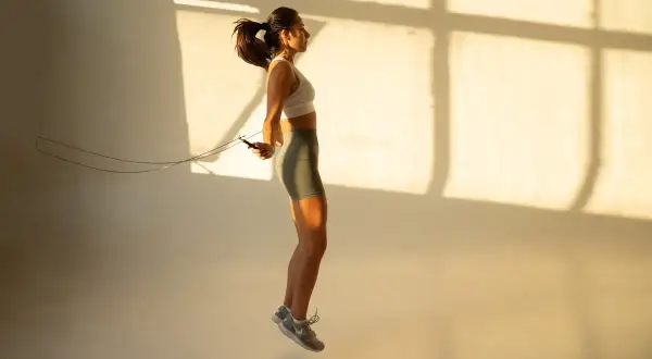 Kobieta w sportowym stroju ćwiczy z **skakanką Adidas**, unosząc się w powietrzu.