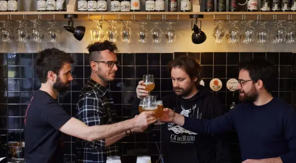 Amici brindano durante una visita birrificio. Bottiglie di birra e bicchieri in primo piano.