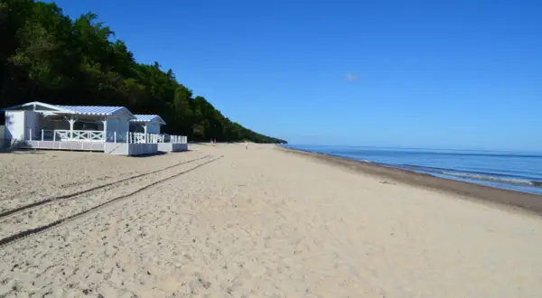 Plaża w Pobierowie z białymi budynkami i niebieskimi markizami, idealne miejsce na wakacyjne atrakcje nad morzem.