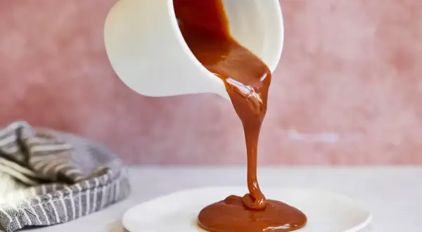 Flüssige Karamellsauce fließt aus einer weißen Kanne auf einen Teller. Ein einfaches karamellsauce rezept für süße Momente.