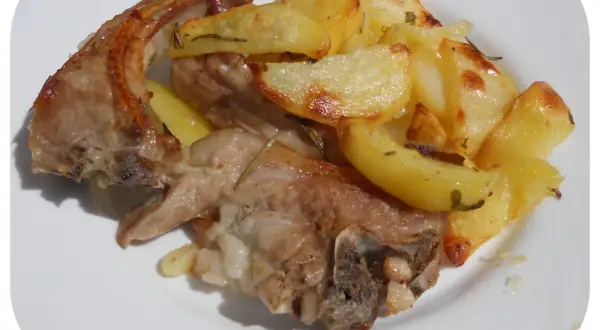 Un succulento agnello gratinato al forno, servito con patate dorate e profumate al rosmarino su un piatto bianco.