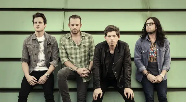 Czterech członków zespołu Kings of Leon siedzi na tle zielonej ściany.