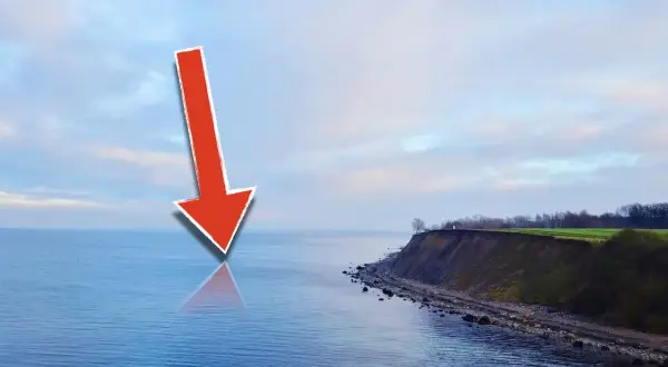 Roter Pfeil zeigt auf die Ostsee, wo sich Meerforellen-Hotspots befinden. Küste mit Steilküppe im Hintergrund.