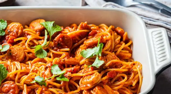 Pyszne spaghetti z kiełbasą w sosie pomidorowym, udekorowane kolendrą. Idealny pomysł, co zrobić z makaronem spaghetti na szybki obiad.