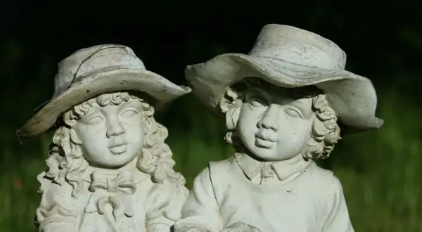 Zwei alte Gartenfiguren aus Stein, Kinder mit Hüten, im Grünen.