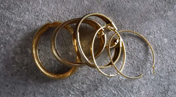 Un grupo de pulseras y aros dorados sobre fondo gris. Aunque el oro no se oxida, estas piezas lucen un brillo que evoca el paso del tiempo.