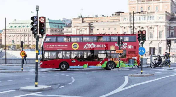 Röd dubbeldäckare för city sightseeing Stockholm passerar en korsning med trafikljus.