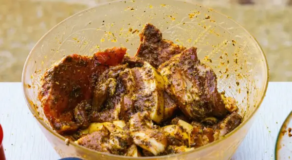 Karkówka w misce, gotowa do grillowania. Aromatyczna marynata do karkówki otula soczyste kawałki mięsa, zapowiadając pyszny posiłek.