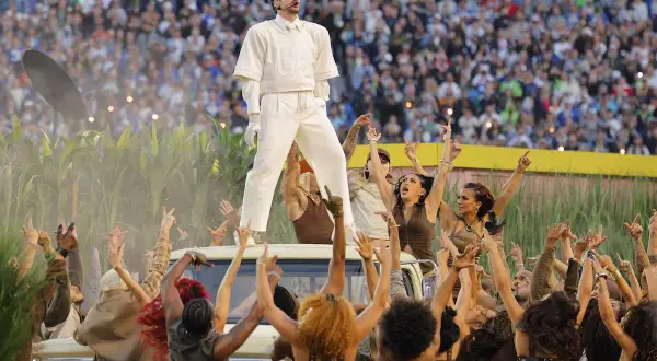 Bad Bunny na Super Bowl, otoczony przez tancerzy i tłum, na tle kukurydzy i stadionu.