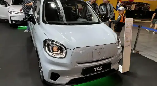 Biały Leapmotor T03 z czarnym dachem, prezentowany na wystawie. Obok samochodu stoją ludzie, w tym chłopiec w czapce.