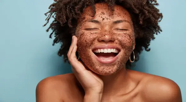 Mujer sonríe con la cara cubierta de exfoliante, mostrando cómo exfoliar la piel para un brillo radiante.