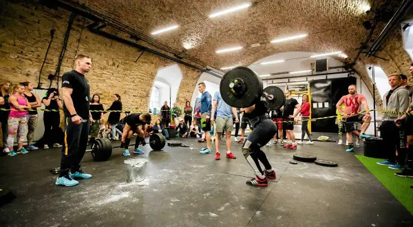 Kobieta podnosi sztangę w siłowni CrossFit, podczas gdy widzowie obserwują.