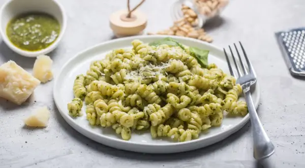 Pyszny makaron z pesto, posypany parmezanem, z dodatkiem świeżej bazylii i orzeszków piniowych.