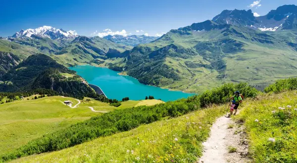 Une personne fait une rando alpes, profitant d'un lac turquoise et de montagnes majestueuses.