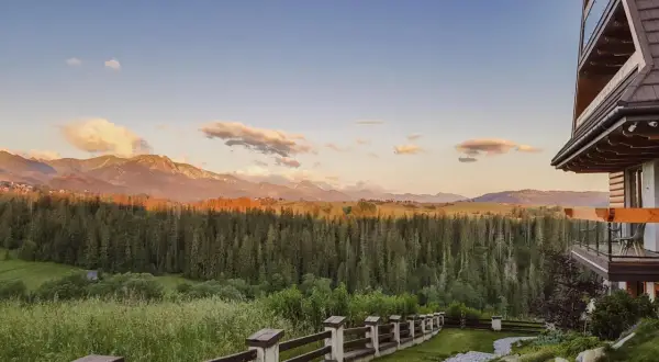 Widok z hotelu Kopieniec Murzasichle na Tatry o zachodzie słońca. Drewniany domek, kamienna ścieżka i las.
