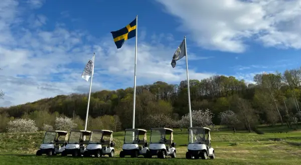 Golfbilar redo för spel vid äppelgården i Båstad. Svenska flaggan vajar stolt i bakgrunden.