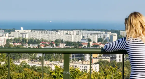 Widok z punktu widokowego w Oliwie na morze i osiedle. Kobieta w bluzce w paski podziwia panoramę.
