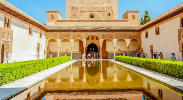 El Patio de los Leones en la Alhambra, con su estanque reflejando la arquitectura y un grupo de visitantes admirando la belleza.