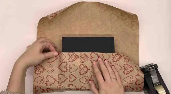 Händer viker hjärtmönstrat papper runt ett svart paket. Snart är det dags att slå in stort paket.