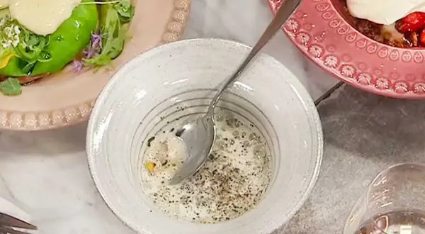 En skål med krämig majs, kryddad med peppar, bredvid en tallrik med grönsaker och en rosa tallrik med jordgubbar och grädde.